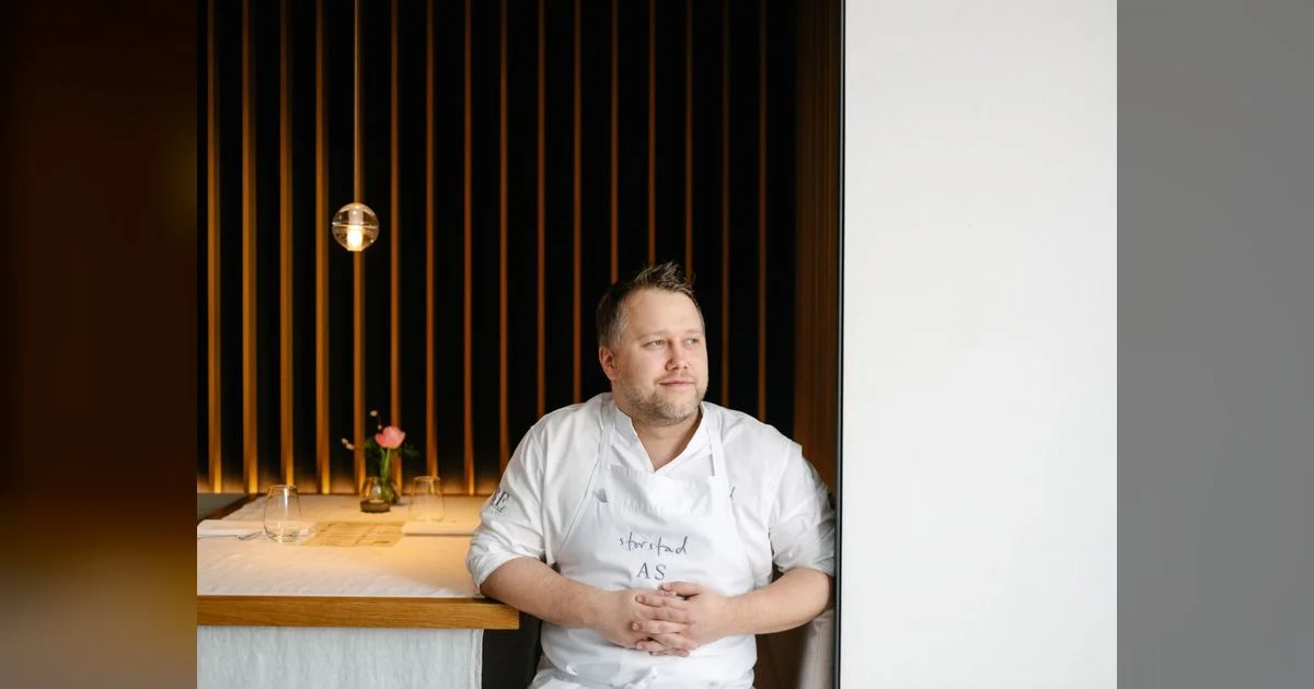 Anton Schmaus in weißer Kochjacke und Schürze am gedeckten Tisch im Restaurant Storstad