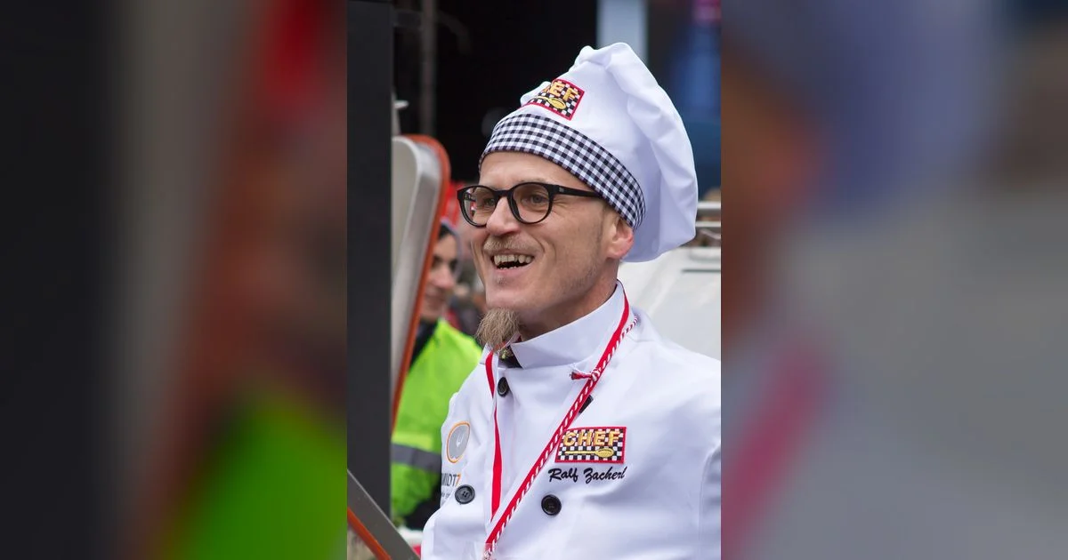 Mann mit Kochmütze und Brille in weißer Kochuniform lächelt bei einer Veranstaltung